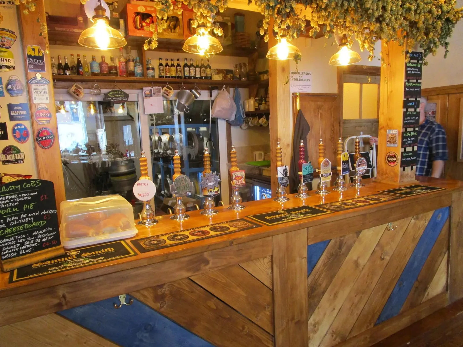 The bar at The Blue Boar — hand pulls, hop bines and the cellar behind glass